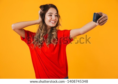 Portrait of a lovely cheerful young woman standing isolated over yellow background, taking a selfie