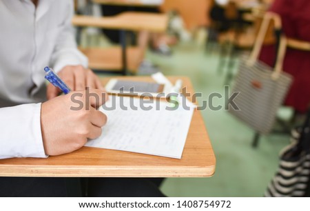 Student using a pen writing or taking lecture notes in the classroom; education concept picture or photo of young learner doing assignment in a career development center of the college or university 