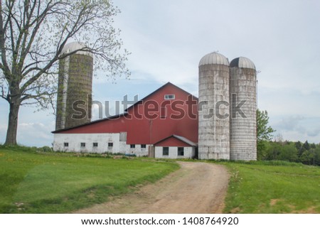 A landscape picture of farm consisting of a red barn surrounded by silos along a scenic Pennsylvania rural road.