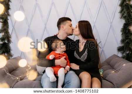 Yound husband kiss his wife with little child on arms