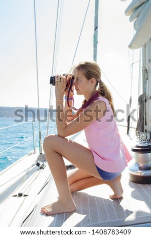 Beautiful teenager young woman on luxury sailing yacht summer vacation using photographic camera, taking picutres against sunny sky, outdoors. Activities leisure recreation lifestyle technology.