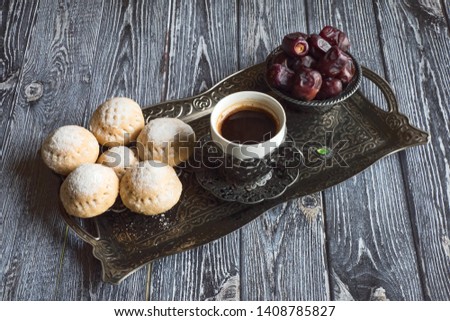 Top view on silver plate with sweets, date fruits and coffee cup on the dark wooden table. Ramadan background.