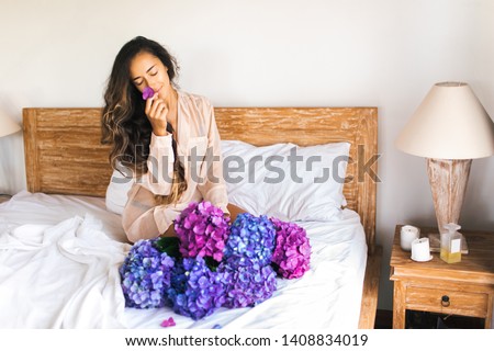 Beautiful woman with huge violet and pink hudrongea bouquet smiling on the bed at home. Romantic morning mood. Good morning.