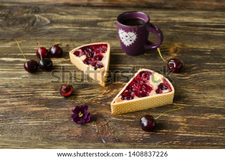 Mini tarts with cherries and cream with cup of black tea on dark wooden background