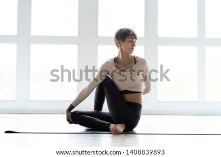 Young attractive woman practicing yoga, sitting in Ardha Matsyendrasana exercise, Half lord of the fishes pose, working out, wearing sportswear