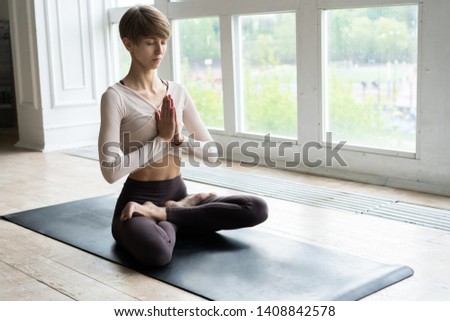 Young attractive smiling woman practicing yoga, sitting in Half Lotus exercise, Ardha Padmasana pose, working out, wearing sportswear