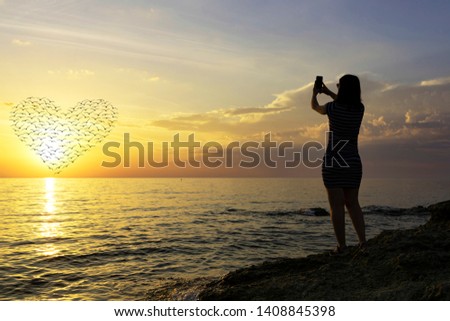 silhouette of a young girl. Photographs a beautiful sunset on the phone. heart of the silhouettes of birds in the sun.
