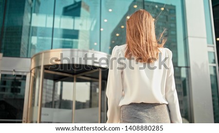 Unrecognizable Slender Caucasian Business Woman Manager in White Shirt is Entering into Office Building via Glass Revolving Door Royalty-Free Stock Photo #1408880285