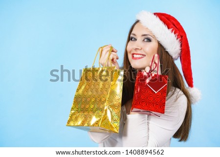Young adult pretty woman is happy to give Christmas gifts. Female wearing red Santa Claus hat holding presents. Blue background