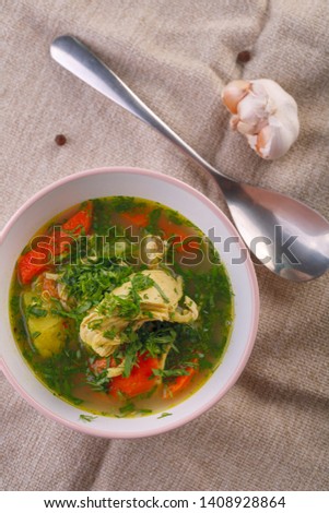 homemade soup with chicken and vegetables with greenery on white table. closeup