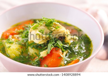 homemade soup with chicken and vegetables with greenery on white table. closeup