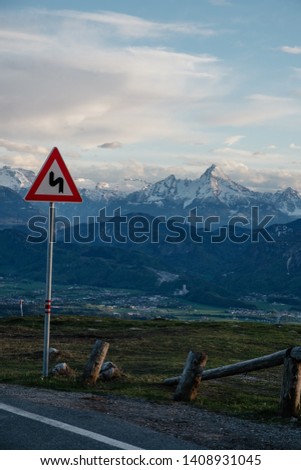 Twisty road ahead sign informing drivers of serpentines in Austria. Gorgeous alpine landscape with road sign on the pole and evening light. Vertical shot.