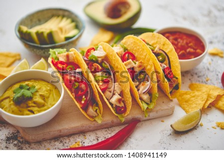 Delicious Mexican fresh crispy tacos are served on wooden board. Stuffed with grilled chicken, spicy pepper, onion, tomato and more. With salsas on side.