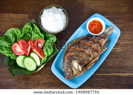 Fried tilapia fish served with lettuce, cucumber, tomato, rice and sambal or chili sauce 