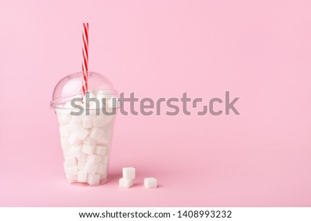 Shake glass with straw full of sugar cubes on pastel pink background. Unhealthy diet concept. Minimal, copy space, side view. Royalty-Free Stock Photo #1408993232