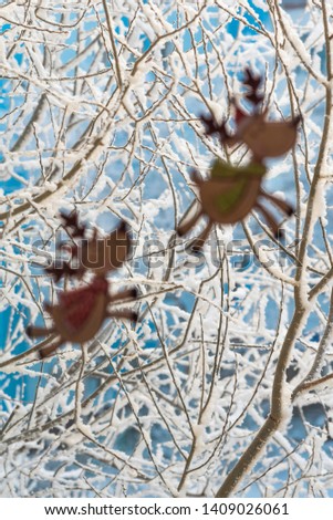 A view from the window on tree branches covered with snow, with two decorative stickers in the form of deer in the blurred foreground. Selective focus.