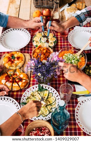 Four adult people enjoying meal together. Red checkered tablecloth in the table outdoor in the terrace. Wooden cutting board with pizza. Vegetables and eggs. Fresh natural fruits