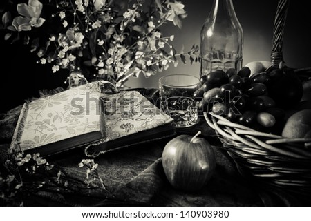 Still life with old books fruits basket and glasses. Black and white photo.