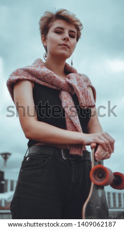 Portrait of young female skateboarder holding her skateboard. Woman with skating board at skate park looking at camera outdoors