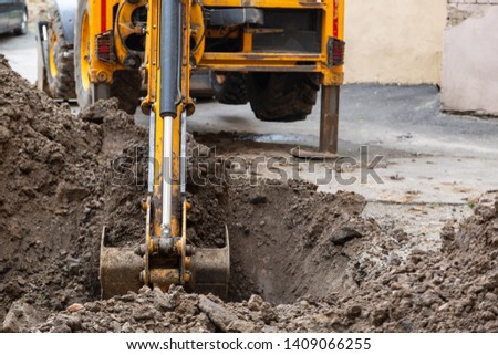 Excavator digs a trench. Repair work in the courtyard of a residential building. Royalty-Free Stock Photo #1409066255