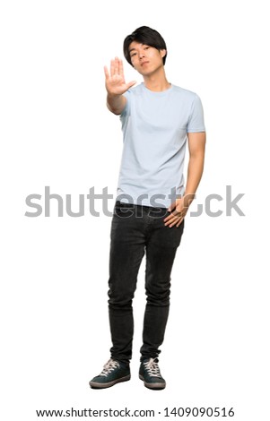 A full-length shot of a Asian man with blue shirt making stop gesture over isolated white background