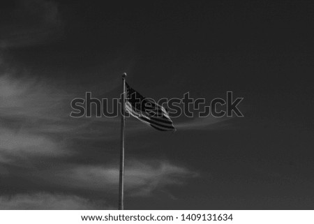 An American flag waving in the wind in front of a mostly clear blue sky, done in black and white. 
