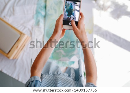 Teenage redhead girl is taking picture of her painting, lying on the floor, with her smartphone. Cropped. Arms only.