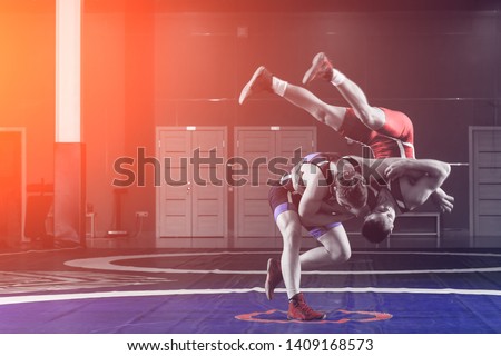 Two young men in blue and red wrestling tights are wrestlng and making a hip throw on a wrestling carpet in the gym. The concept of fair wrestling