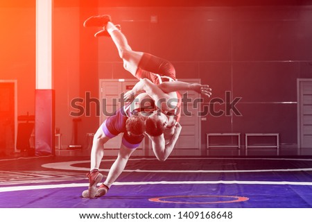 Two young men in blue and red wrestling tights are wrestlng and making a suplex wrestling on a wrestling carpet in the gym. The concept of fair wrestling