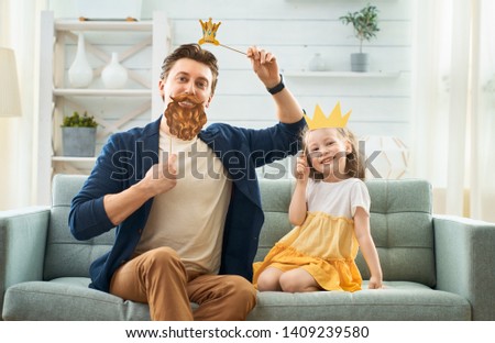 Funny family! Father and his child daughter with a paper accessories. Funny girl holding crown on stick. 
