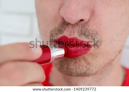 Portrait,   man with a bristle applying colorful red lip  lipstick on his lips, side view, close up