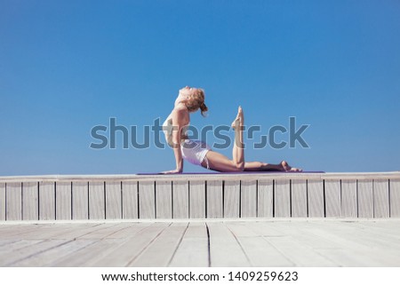 Sporty young woman doing upward facing dog exercise, Urdhva mukha shvanasana pose. Slim girl practicing yoga outdoor, blue sky, white sportwear, wooden terrace. Calm, relax, healthy lifestyle concept