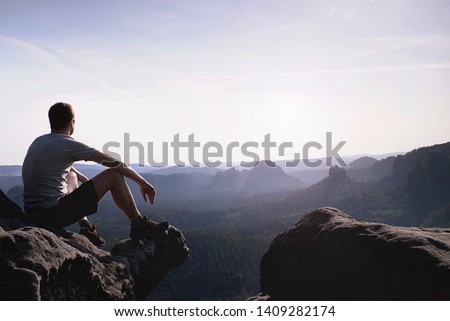 Thinking man sit on rock. Man on exposed summit watching to misty far distance. Cold day in mountains.