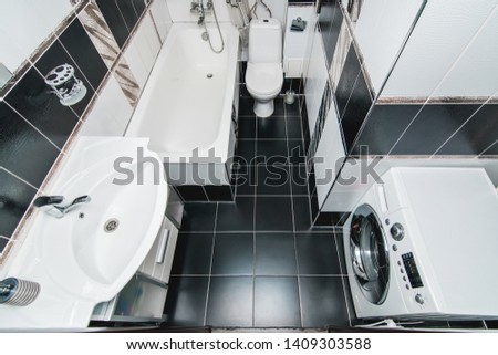 Bright picture of a bathroom with white clean bathroom with ceramic tiles with toilet sink washing machine and shower