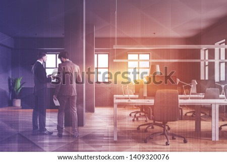 Two businessmen discussing documents in modern industrial style office with gray walls, wooden floor and row of white computer desks. Reception counter in background. Toned image double exposure