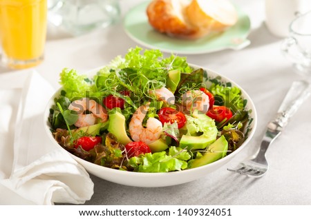 Fresh summer salad with shrimp, avocado and tomato cherry in bowl on light table. Concept of healthy eating. Royalty-Free Stock Photo #1409324051