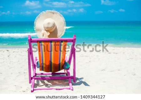 Journey. On the beach, a girl sits in a colored pareo and straw hat with her back to the camera in a beach chair, relaxation, relaxation and sunbathing.