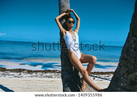 A woman in a white swimsuit leaned her back on a tree trunk glasses tan sea island               