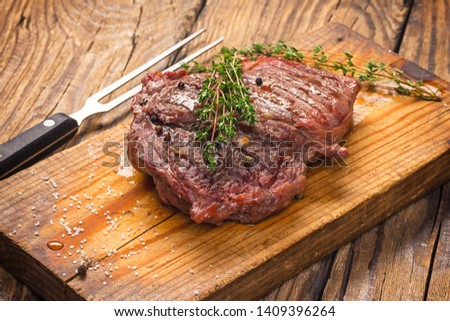 Juicy medium rare beef steak on wooden board with herbs spices and salt.