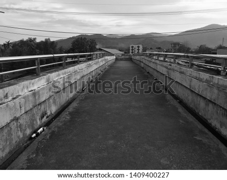 A black and white picture of pedestrian walkway With a background is wires, mountains and sky.
