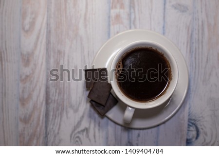 Black coffee in a white Cup with a saucer and pieces of chocolate on the table top view, background for text