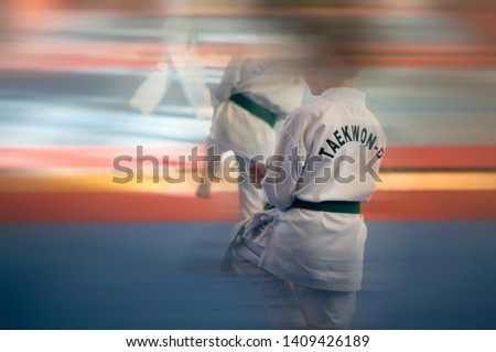 martial arts blurred background. A young man in a white kimano with a green belt. Demonstrates Taekwondo Tuli. Text on kimono "Taekwondo"