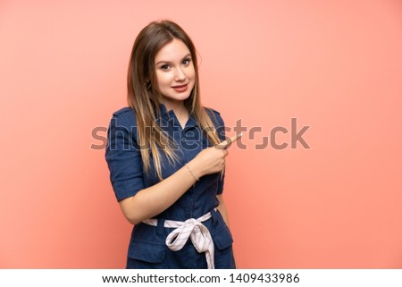 Teenager girl over isolated pink background pointing to the side to present a product