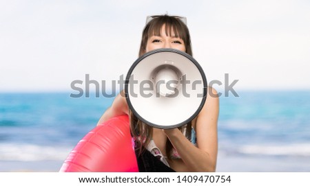 Young woman in bikini shouting through a megaphone at the beach