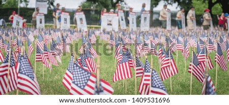 Panorama view lawn American flag with row of people from Memorial Day March event in Dallas, Texas, USA. Blurry crowded family members carry fallen heroes banners pictures placards in parade