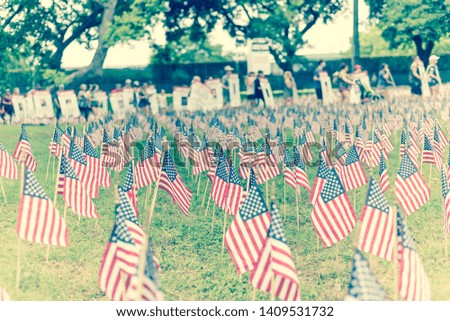 Vintage tone close-up lawn American flag with row of people from Memorial Day March event in Dallas, Texas, USA. Blurry crowded family members carry fallen heroes banners pictures placards in parade