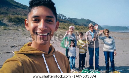Young man taking selfie to group of volunteers after cleaning the beach