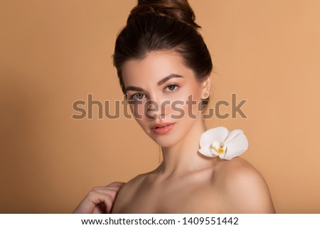 Closeup portrait of young beautiful girl with flawless skin with white orchid flower on her shoulder. Skin care, beauty and cosmetics concept.