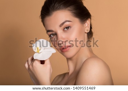 Young beautiful girl with flawless skin is holding white orchid flower on her hands. Skin care, beauty and cosmetics concept.