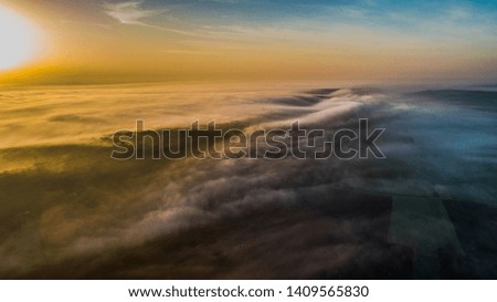 Aerial view of green fields covered with fog during sunrise